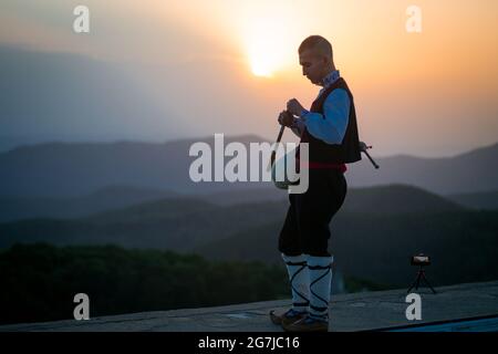 Ein junger Dudelsackläufer in Volkstracht spielt auf einem Berggipfel, wenn die Sonne aufgeht, am 01. Juli 2021, Shipka, Bulgarien Stockfoto