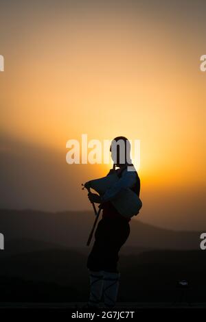 Ein junger Dudelsackläufer in Volkstracht spielt auf einem Berggipfel, wenn die Sonne aufgeht, am 01. Juli 2021, Shipka, Bulgarien Stockfoto