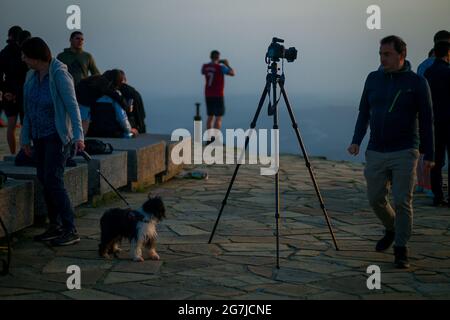 Junge Leute, Fotografen und ein Welpe auf einem Berggipfel erwarten den Sonnenaufgang - July Morning am 01. Juli 2021 Stockfoto