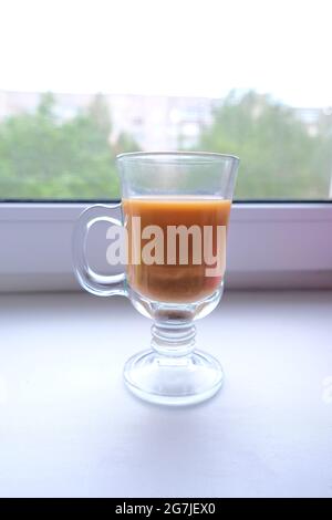Kaffee mit Milch in einer transparenten Tasse auf der Fensterbank Stockfoto