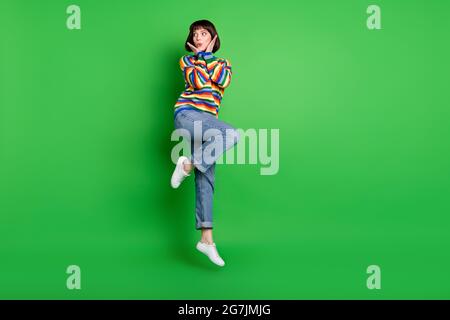 In voller Länge Foto von ziemlich beeindruckt Frau tragen Pullover springen hohe Arme Wangen leeren Raum isoliert grüne Farbe Hintergrund Stockfoto