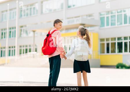 Zurück in die Schule, zwei glückliche Kinder sind bereit für die Grundschule, Schüler am ersten Tag der Schule, ein Junge und ein Mädchen gehen Hand in Hand, um den Unterricht mit b Stockfoto