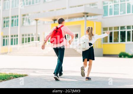 Zurück in die Schule, zwei glückliche Kinder sind bereit für die Grundschule, Schüler am ersten Tag der Schule, ein Junge und ein Mädchen gehen Hand in Hand, um den Unterricht mit b Stockfoto