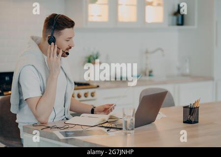 Junger Mann, der das Headset anpasst, während er zu Hause online lernt Stockfoto