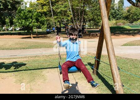 8-jähriges Kind, in einem blauen Hemd, springt an einem sonnigen Tag von einer Schaukel. Stockfoto