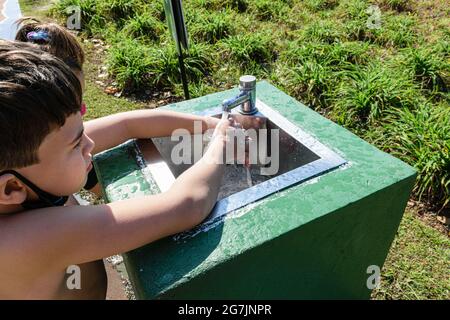 8-jähriges Kind, das sich in einem Waschbecken im Freien in einem öffentlichen Park die Hände wäscht. Stockfoto