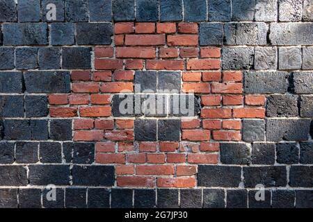 Rotes Ziegelmuster auf der schwarzen Schlackensteinmauer einer alten Mühle im Dorf Fiskars in Raasepori, Finnland Stockfoto