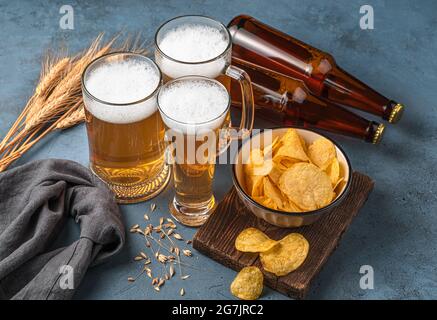 Drei Bierbecher, Chips und Bierflaschen auf dunkelblauem Hintergrund. Stockfoto