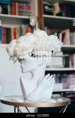 Ein Haufen weißer Pfingstrosen in einer Vase mit menschlichem Kopf Stockfoto