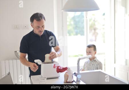 Erwachsener Vater, der morgens ein Sandwich für seinen Sohn in der Küche zubereitet Stockfoto