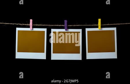 Leere quadratische Bilderrahmen, die auf einer Wäscheleine mit schwarzem Hintergrund hängen Stockfoto