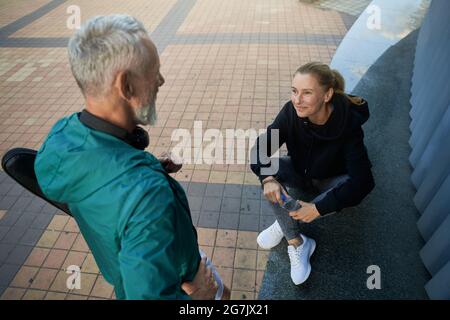 Ein Blick aus dem Blickfeld auf ein sportliches reifes Paar, einen Mann und eine Frau in Sportkleidung, die im Freien reden, während sie gemeinsam auf das Training warten Stockfoto