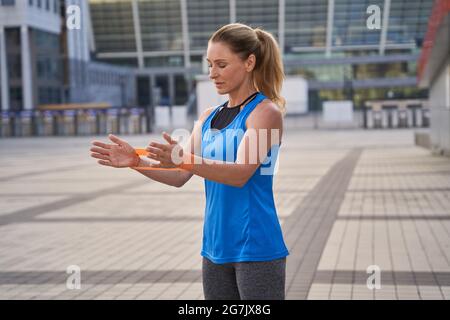 Fokussierte sportliche Frau in Sportkleidung, Trainerin mit Widerstandsband, während sie im Freien steht und in der Stadt trainiert Stockfoto