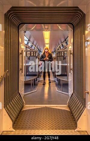 Blonde Frau mit Sonnenbrille und Gesichtsmaske, die im Auto des Zuges steht und auf die Kamera schaut. Stockfoto