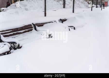 Reihe von städtischen Holzbänken in Schneeverwehungen mit Schnee nach starkem Schneefall bedeckt Stockfoto