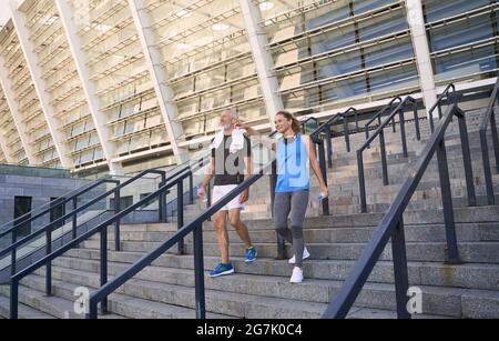 Aktives reifes Paar, Mann und Frau in Sportkleidung, die Gespräche führen, während sie nach dem gemeinsamen Training im Freien die Treppe hinuntergehen Stockfoto
