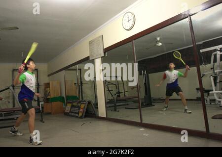 Im Jaya Raya Badmintonclub in Jakarta, Indonesien, übt ein junger Badmintonathlet verschiedene Schläge vor einem großen Spiegel. Stockfoto