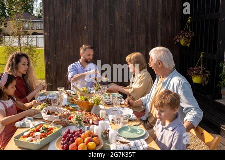 Große Familie essen leckeres Essen an einem großen Tisch im Hinterhof des Ferienhauses am sonnigen Sommertag Stockfoto