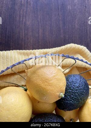 Vertikale Draufsicht auf frische Zitronen und Avocados in einer Metallschüssel auf einem gelben Handtuch in der Küche Stockfoto