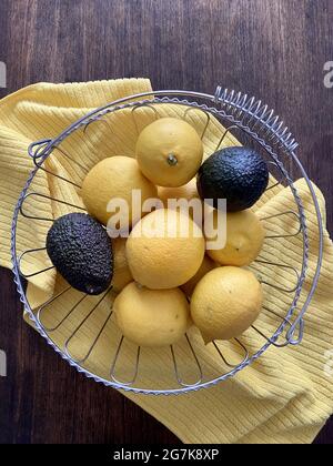 Vertikale Draufsicht auf lebendige Zitronen und Avocados in einer Metallschüssel auf einem gelben Handtuch in der Küche Stockfoto