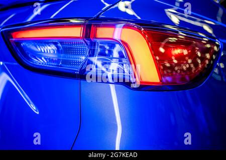 Fragment der eingeschwenkten Glasrückleuchte des blau glänzenden Autos mit Neonlichtreflexion und Blendung der umgebenden Objekte auf dem kombinierten Relief Stockfoto