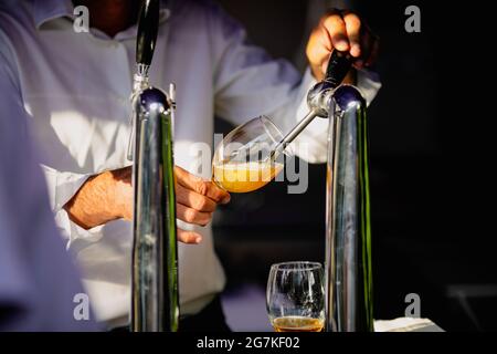 Bild mit geringer Schärfentiefe (selektiver Fokus), bei dem ein Mann Craft-Bier aus einem Spender in ein Glas gießt. Stockfoto