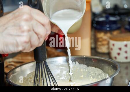 Der Koch gibt Milch in eine Teigschüssel, um Backwaren mit Spargel und Erbsen zu machen. Schritt für Schritt Rezept. Stockfoto