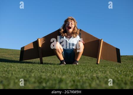 Kind, das im Flugzeug fliegt, machte Handwerk aus Pappflügeln. Traum, Phantasie, Kindheit. Reise- und Sommerurlaubskonzept. Lächelndes Kind, das davon träumt Stockfoto