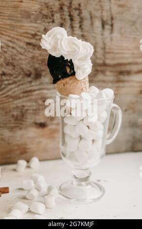 Schokoladeneis in einem Kegel in einem Glas mit Marschmalchen auf einem Holzhintergrund. Süßes Dessert auf dem Tisch. Zusammensetzung mit Eis Süßer Snack. Stockfoto
