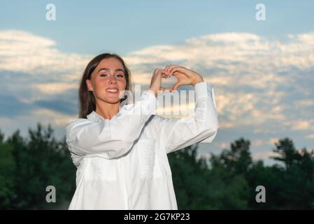 Junge Frau, die bei Sonnenuntergang eine Hand in Herzform auf einem Garten macht. Frau in der Natur hält Herz-Form-Symbol mit Hands.Love und Natur Beauty-Konzept gemacht Stockfoto