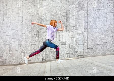 Sportliche, reife Frau joggt in einem gesunden, aktiven Outdoor-Lifestyle- und Fitnesskonzept durch die Stadt, die an Geschäftsgebäuden vorbeiläuft Stockfoto
