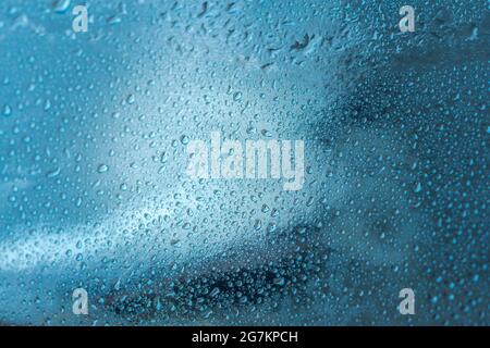 Abstrakter Hintergrund mit Regentropfen und schönem blauen Bokeh. Das Konzept des Herbstes und des kalten stürmischen Wetters. Textur von Makrotropfen auf dem verschwommenen Stockfoto