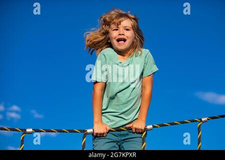 Portrait von niedlichen Jungen Kind tun Klettern und Affen Bars im Hintergrund. Lustige Kinder Gesicht. Stockfoto