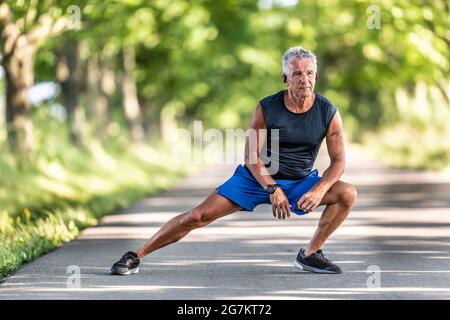 Der grauhaarige alte Mann, der noch in Form ist, streckt die Beine in seinem Aufwärmpuls vor dem Training. Stockfoto