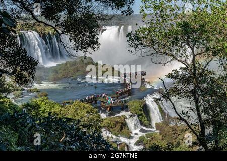 Touristen drängen sich auf einer Promenade, um von der brasilianischen Seite aus eine Nahaufnahme der Iguazu-Wasserfälle zu erhalten Stockfoto