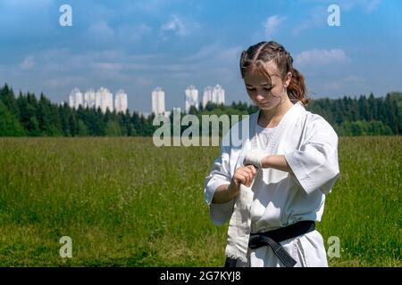 Teenager-Mädchen in einem Kimono wickeln ein Handgelenk um ihre Hand, bevor sie im Freien Karate-Training beginnen Stockfoto