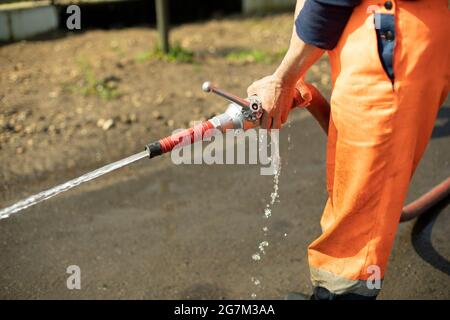 Wasserschlauch. Der Wasserfluss aus dem Rohr. Ein Mann hält einen Feuerwehrschlauch. Stockfoto