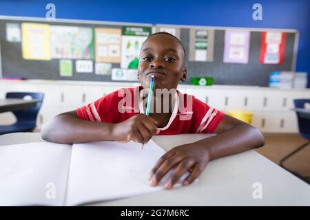 Porträt eines afroamerikanischen Jungen, der in der Grundschule auf seinem Schreibtisch sitzt Stockfoto