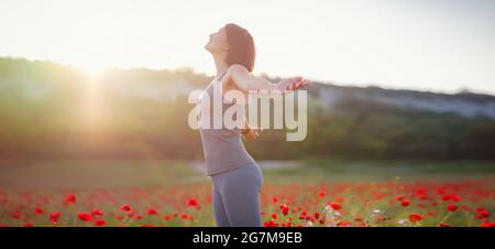 Junge schöne Frau mit erhobenen Armen im Frühjahr Mohnfeld. Sanfte Farben. Nachdenkliche, entspannte Atmosphäre. Stockfoto