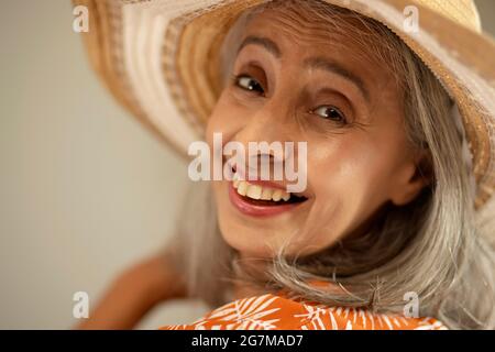 Eine glückliche alte Frau, die Freude mit einem Hut bekundet. Stockfoto