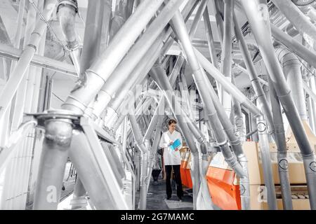 Moderne elektrische Mühlenmaschinen für die Produktion. Der Bediener überprüft die Qualität der Fertigprodukte Weizenmehl. Stockfoto