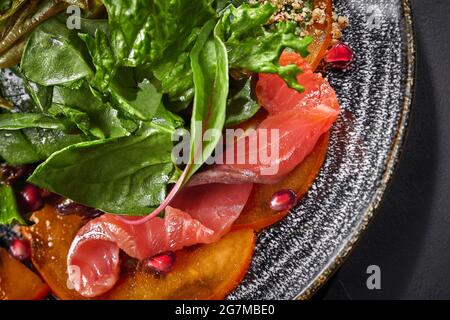 Nahaufnahme von Salat aus Kaki, Lachs, Grüns, Granatapfel, Walnüssen Stockfoto
