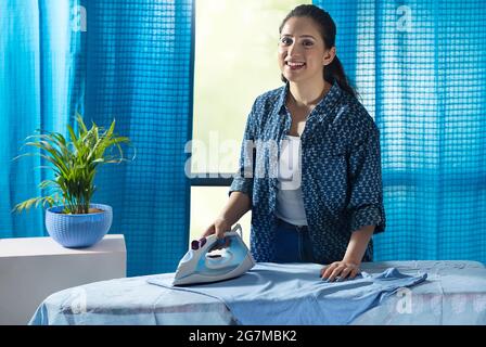 Eine Frau, die ihre Kleider in ihrem Zimmer bügelt. Stockfoto