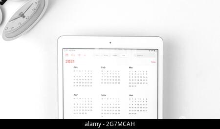 Tablet mit offenem Kalender 2021, Arbeitsbereich mit weißem Hintergrund und Wecker, Geschäftskonzept Stockfoto