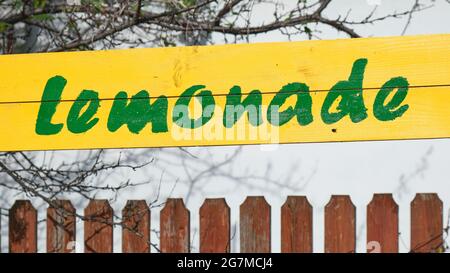 Grüner Lemonade handgeschriebener Text auf gelbem Holzschild, neben einem Zaun. Sommer frische Getränke, Getränke. Stockfoto