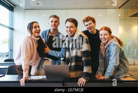 Fröhliche Gruppe von Schülern, die in einem Klassenzimmer Spaß haben und die Kamera betrachten. Junge Menschen in einem Klassenzimmer. Stockfoto