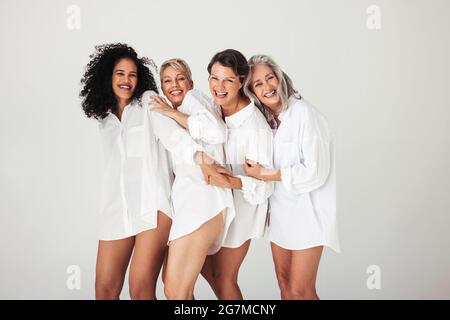 Studioaufnahme verschiedener weiblicher Models, die ihren natürlichen und alternden Körper umarmen. Vier selbstbewusste und glückliche Frauen lächeln fröhlich, während sie weiß tragen Stockfoto