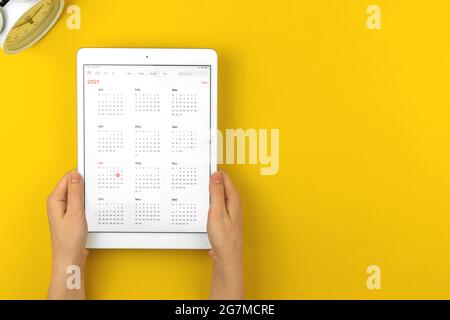 Kalender 2021 auf Tablet, gelber Desktop und Arbeitsbereich, Draufsicht Stockfoto