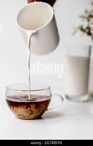Vertikale Aufnahme einer Hand, die Milch auf einen Kaffee gießt Stockfoto