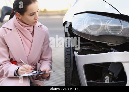 Eine Expertin füllt Dokumente in der Nähe eines kaputten Autos auf der Straße aus Stockfoto